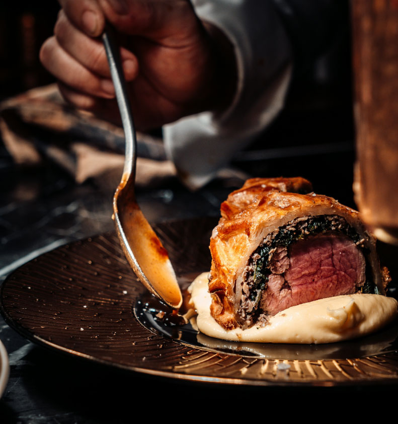 person holding stainless steel fork and knife slicing meat on black ceramic plate